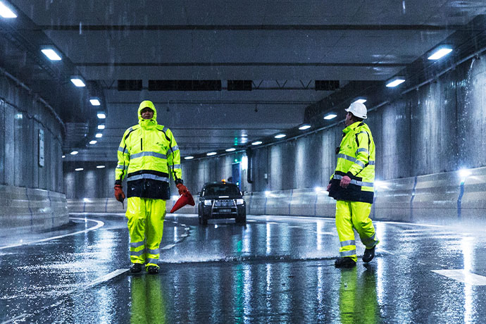 Two people in high-visibility clothing in a tunnel and a car in the background