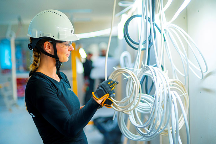 Installation of electrical cables is carried out by employees wearing helmets and protective gloves.