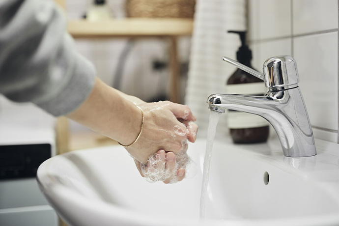 Bilden visar en person som tvättar sina händer i ett tvättställ