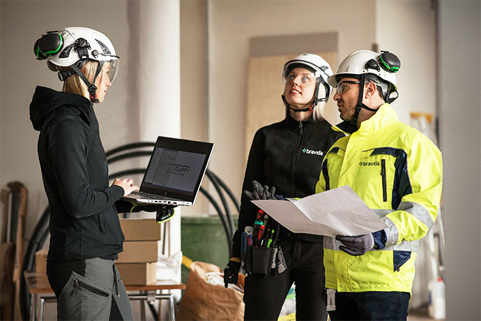 Tre medarbetare i en diskussion på en byggarbetsplats